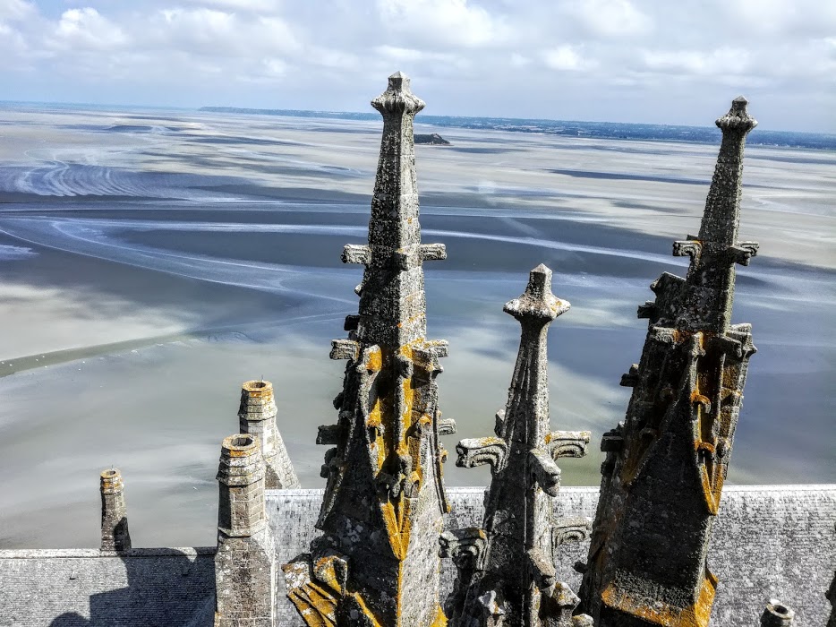 Mont-Saint-Michel, entre 2 pinacles au sommet de l'abbaye, on aperçoit l'îlot de Tombelaine qui se dresse au milieu des grèves à 2,3 km au nord. Lorsque le temps est clair, on distingue les îles Chausey d'où provient le granite qui servit à la construction de l'abbaye (Photo FC)
