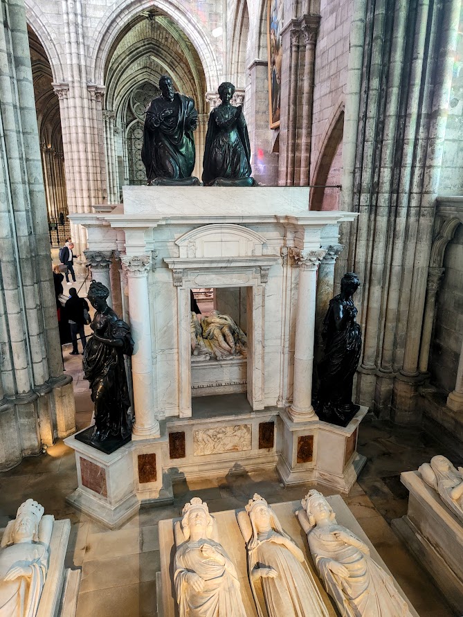 Tombeau d’Henri II et de Catherine de Médicis, l’un des plus majestueux édifices funéraires de la basilique. Il a été commandé, en 1560, à Germain Pilon et Ponce Jacquiot, par le Primatice qui travaillait pour François Ier (maître incontesté de l’école dite de Fontainebleau). Les deux gisant sont situés dans une chapelle du chevet nord, sculptés en vêtement de sacre. Ils ont les yeux grands ouverts. Cet monument conçu comme un temple à l'antique est doté de marbres de différentes couleurs, Voir les monumentales vertus de bronze aux quatre angles du tombeau (prudence, force, tempérance et justice). Au sommet, les figures agenouillées sont en habit de sacre. Le roi tient sa main droite sur le cœur en allégeance à sa foi catholique.




Tombeau d’Henri II et de Catherine de Médicis, l’un des plus majestueux édifices funéraires de la basilique. Il a été commandé, en 1560, à Germain Pilon et Ponce Jacquiot, par le Primatice qui travaillait pour François Ier (maître incontesté de l’école dite de Fontainebleau). Les deux gisant sont situés dans une chapelle du chevet nord, sculptés en vêtement de sacre. Ils ont les yeux grands ouverts. Cet monument conçu comme un temple à l'antique est doté de marbres de différentes couleurs, Voir les monumentales vertus de bronze aux quatre angles du tombeau (prudence, force, tempérance et justice). Au sommet, les figures agenouillées sont en habit de sacre. Le roi tient sa main droite sur le cœur en allégeance à sa foi catholique.
